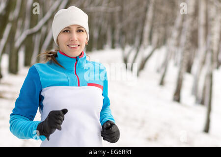 Fröhliche junge Sportlerin Joggen im Winter im Freien. Lächelnde kaukasische Mädchen laufen in Winter park Stockfoto