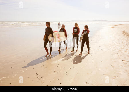 Vier junge glücklich Surfer zu Fuß den Strand mit Surfbrettern Stockfoto