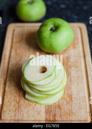 Ein Kochapfel in Scheiben geschnitten und auf ein Schneidebrett mit zwei ungeschnittene Äpfel hinter entkernt. Stockfoto