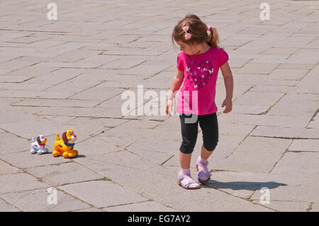 Junges Mädchen mit rosa t-Shirt mit Herzen und Blumen geschmückt zieht zwei Spielzeughunde auf String in Campo San Stefano Venedig Italien Stockfoto