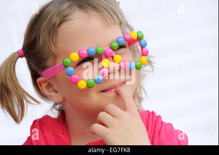 Porträt der niedliche kleine Mädchen tragen lustige Brillen, verziert mit bunten Süßigkeiten, Smarties, Bonbons. Sieben Jahre altes Kind Stockfoto