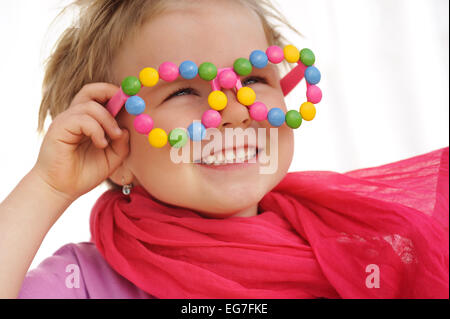 Porträt der niedliche kleine Mädchen tragen lustige Brillen, verziert mit bunten Süßigkeiten, Smarties, Bonbons. Vier Jahre altes Kind Stockfoto