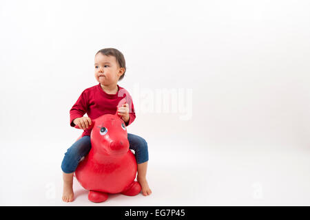 kleines Mädchen auf einem Spielzeugpferd auf weißem Hintergrund Stockfoto