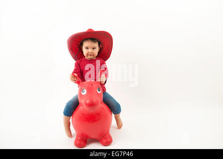 Kleines Mädchen mit roten Cowboyhut auf o Spielzeugpferd isoliert Stockfoto