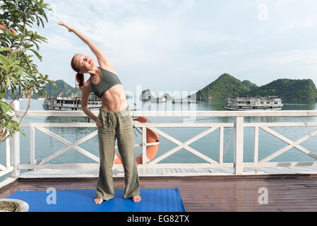 Junge Frau praktizieren Yoga auf dem oberen Deck des Schiffes. Morgen mal kurz nach Sonnenaufgang Stockfoto