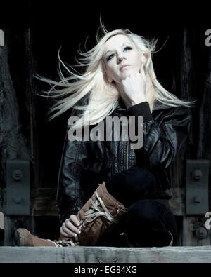 Blondes Mädchen in Stiefel und Lederjacke sucht in einer industriellen Umgebung. Stockfoto
