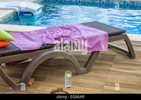 Liegestuhl mit lila Handtuch in der Nähe von Schwimmbad Stockfoto
