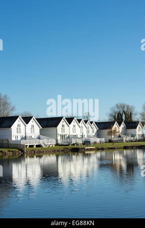 Filmklappe Stil Häuser entlang eines Sees im Wasserzeichen Club, Cotswold Water Park, Gloucestershire, England Stockfoto