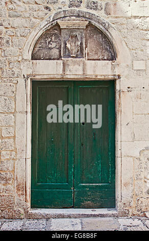 Alten Portals mit einem grünen Holztür, umhüllt von einer weißen Steinmauer, bekrönt von einem Marmor Bogen mit geschnitzten Schild. Stockfoto