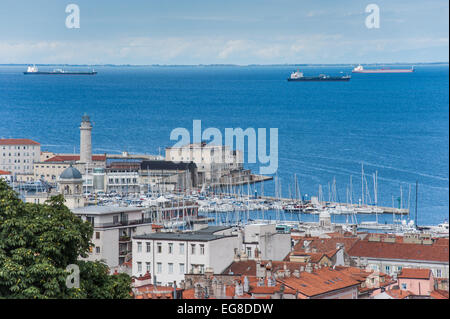 Triest, Italien - ein Blick auf den Hafen mit dem Leuchtturm von San Giusto Kathedrale gesehen. Schiffe in den Straßen vor der Küste. Stockfoto