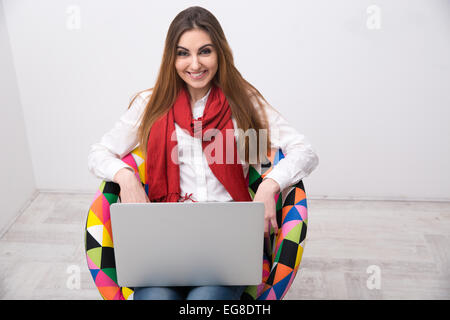 Lächelnde Frau sitzen auf dem bunten Stuhl mit laptop Stockfoto