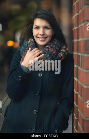 Stilvolle Pretty Young Woman im Herbst Mode stützte sich auf Säule aus rotem Backstein, in die Kamera schaut. Stockfoto