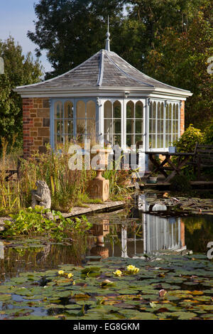 Großer Gartenteich im Sommer mit gemauerten Gartenhaus und Sitzgelegenheiten mit Blick auf Wasser und Lillypads, Garten, Oxfordshire, England Stockfoto