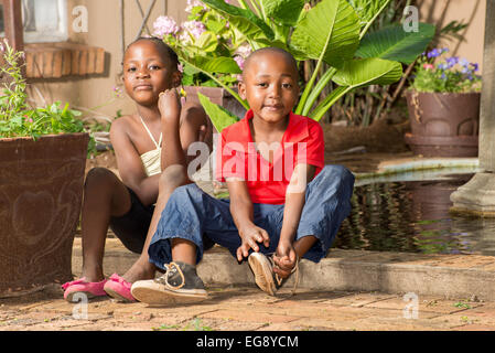Junge fesselt seine Schnürsenkel nachdem er und seine Zwillingsschwester spielte am Teich von ihrem Haus. Stockfoto