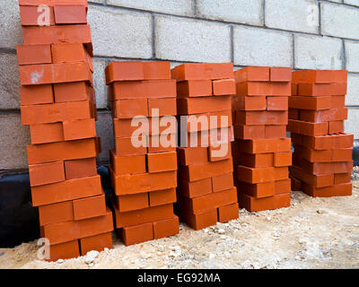 Rote Ziegel aufgeschichtet bereit, auf eine Baustelle mit Breezeblock Wände sichtbar hinter gelegt werden Stockfoto