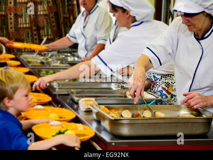 Kinder im Grundschulalter im Vereinigten Königreich Mittagessen von Personal in der Schulküche gekocht serviert wird Stockfoto
