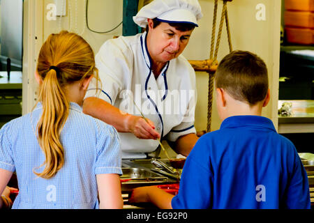 Kinder im Grundschulalter im Vereinigten Königreich Mittagessen von Personal in der Schulküche gekocht serviert wird Stockfoto