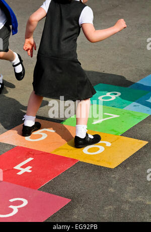 Grundschulkinder spielen auf einem Schulhof in den Pausen mit Himmel und Hölle Spiel markiert auf der Asphaltdecke Stockfoto