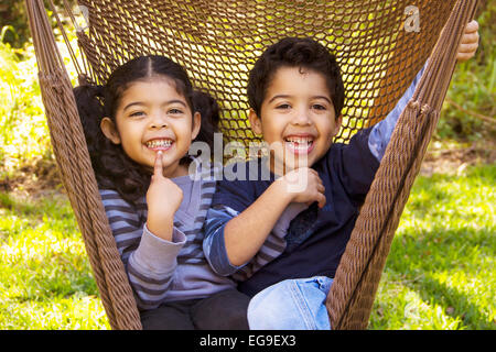 Zwillingsbruder und Schwester sitzen in einer Hängematte, lustige Grimassen Stockfoto
