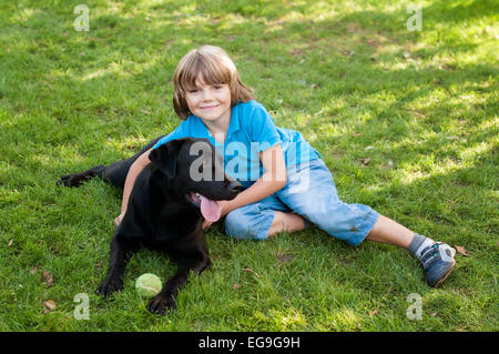 Junge (6-7) auf Rasen liegend mit Hund Stockfoto