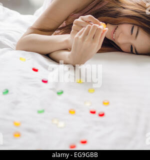 Lächelnde Frau, die auf einem Bett liegt und Süßigkeiten isst