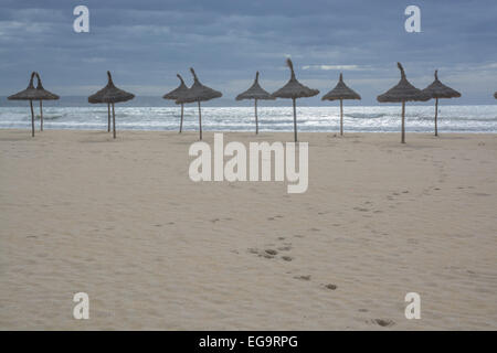 Sandstrand mit Fußweg hinunter zum Wasser und dekorative Stroh Sonnenschirme in einer geraden Reihe. Stockfoto