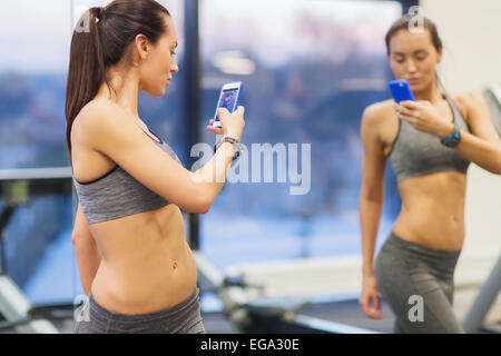 Frau mit Smartphone unter Spiegel Selfie im Fitness-Studio Stockfoto