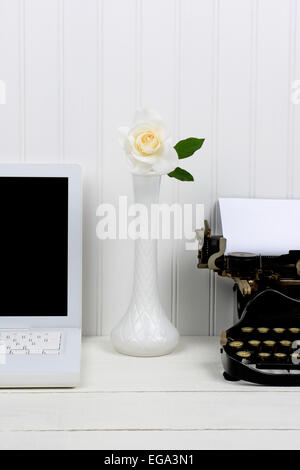 Nahaufnahme von einem weißen Schreibtisch mit einer Knospe Vase zwischen einem modernen Laptop-Computer und eine antike Schreibmaschine. Nur die Hälfte des Laptops und Stockfoto