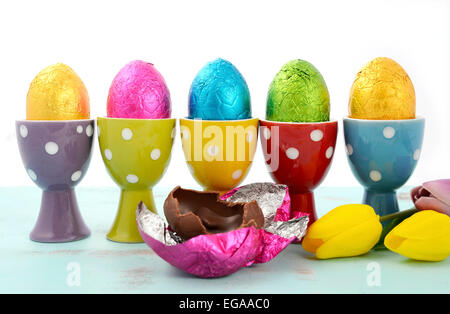Happy Easter-Reihe von Schokoladeneier eingehüllt in helle Farbe Folie in rot, gelb, blau, grün und lila Tupfen Eierbecher. Stockfoto