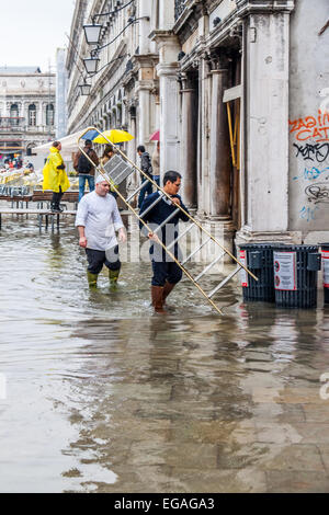 Arbeiter gehen über ihr Geschäft bei Hochwasser (Acqua Alta) in Markusplatz, Venedig Italien Stockfoto