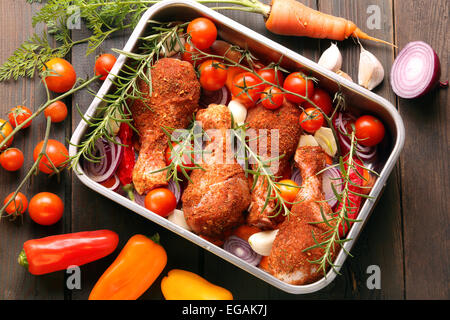 Hähnchen-Drumsticks vorbereitet zum Braten in einer Pfanne mit Gemüse auf einem hölzernen Hintergrund Stockfoto