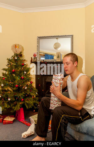 Ein junger Mann öffnet Weihnachtsgeschenke am Weihnachtstag, Sussex, England Stockfoto