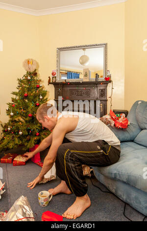 Ein junger Mann öffnet Weihnachtsgeschenke am Weihnachtstag, Sussex, England Stockfoto