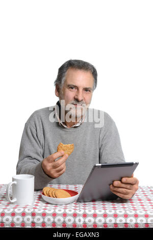 Mann mittleren Alters mit einem Tablet-Computer während des Essens Milch und Kekse zu Hause Stockfoto
