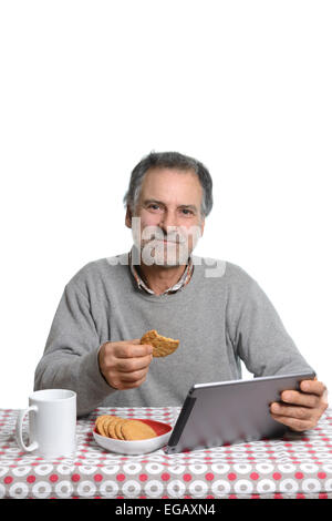 Mann mittleren Alters mit einem Tablet-Computer während des Essens Milch und Kekse zu Hause Stockfoto