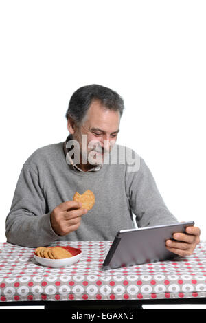 Mann mittleren Alters mit einem Tablet-Computer während des Essens Cookies zu Hause Stockfoto