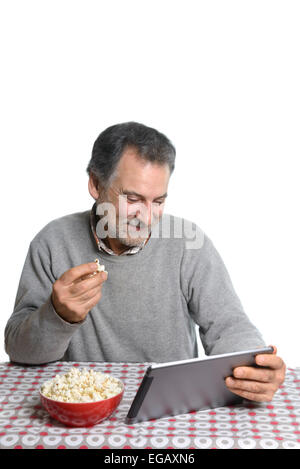 Mann mittleren Alters mit einem Tablet-Computer beim Essen Popcorn zu Hause Stockfoto