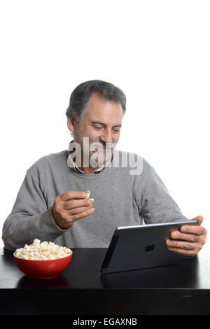 Mittleren Alter Mann mit einer Apple-Tablet iPad Luft beim Essen Popcorn zu Hause Stockfoto