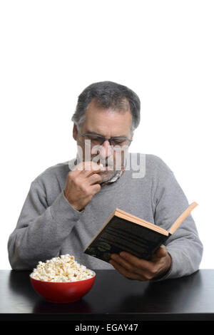 Mann mittleren Alters, ein Buch zu lesen, während des Essens Popcorn zu Hause Stockfoto