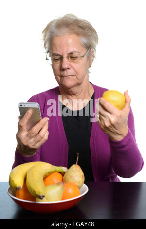 Mittlere gealterte Frau mit einem Apple iPhone beim Verzehr von Obst Stockfoto
