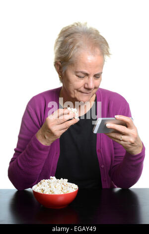 Mittlere gealterte Frau Essen Popcorn beim Ansehen eines Films auf einem Apple iPhone Smartphone Stockfoto