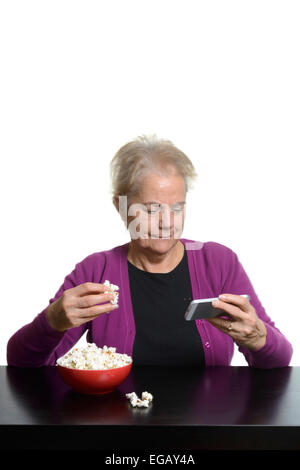 Mittlere gealterte Frau Essen Popcorn beim Ansehen eines Films auf einem Apple iPhone Smartphone Stockfoto