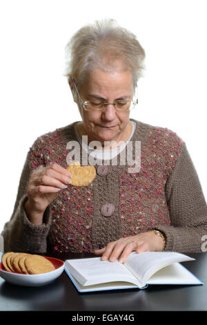 Mittlere gealterte Frau ein Buch zu lesen, während des Essens Cookies zu Hause Stockfoto