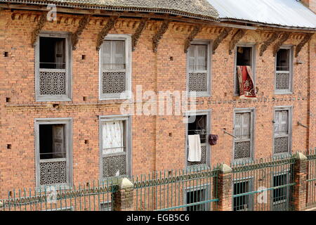 Traditionellen Stil Teppiche hängen, roten Backsteinmauern der traditionellen Newar Stil Gebäude-Farbe verblasst Fenster und Dach streben. Stockfoto