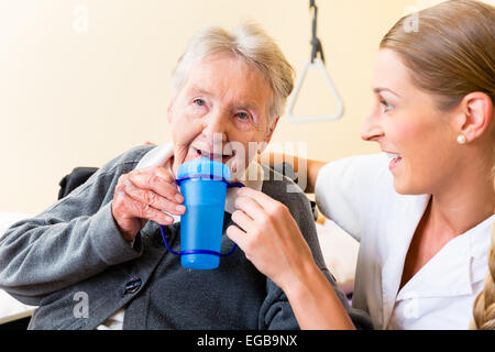 Krankenschwester im Pflegeheim Seniorin im Rollstuhl sitzen und trinken verleiht Stockfoto