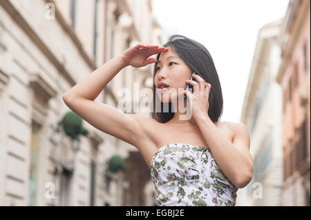 Junge schöne asiatische Frau schaut sich um und sprechen über Handy urban outdoor Frühjahr dressing Stockfoto