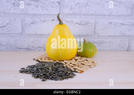 Bunte dekorative Kürbisse und Kürbiskernen auf einem Holztisch mit einer Mauer im Hintergrund Stockfoto