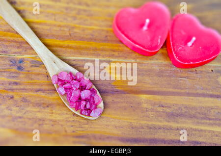 Rosa gefärbt Meersalz in einem Holzlöffel auf einem Holztisch mit herzförmigen Kerzen Stockfoto