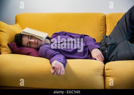 Über-arbeitete, müder junger Mann zu Hause schlafen unter Buch Stockfoto