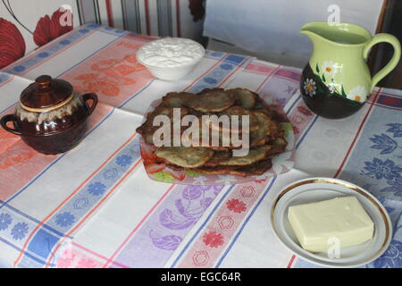 schöne Tradition Kartoffelpuffer auf Teller mit gelben Butter, Sauerrahm, Krug mit Kuhmilch Stockfoto